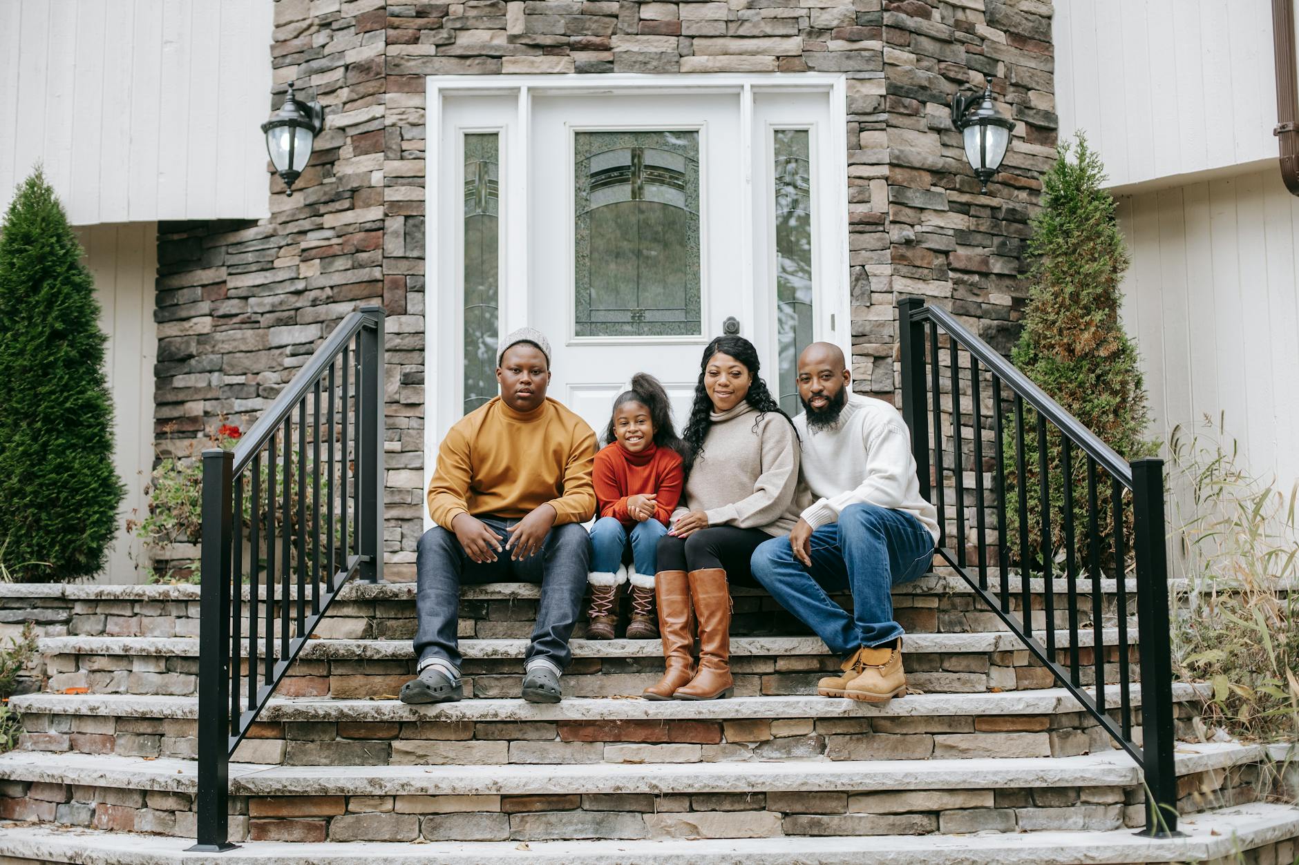 A cheerful family of four sitting on stone stairs outside their house, enjoying a sunny day.