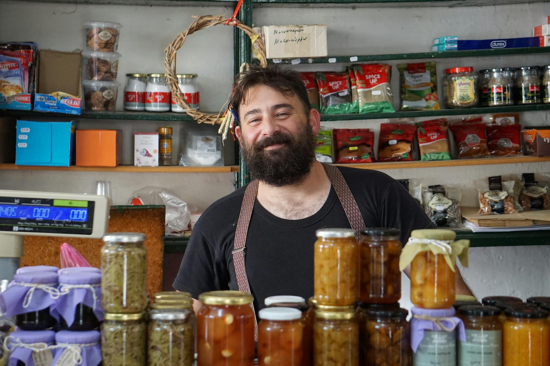 A friendly shopkeeper stands behind shelves of homemade preserves.