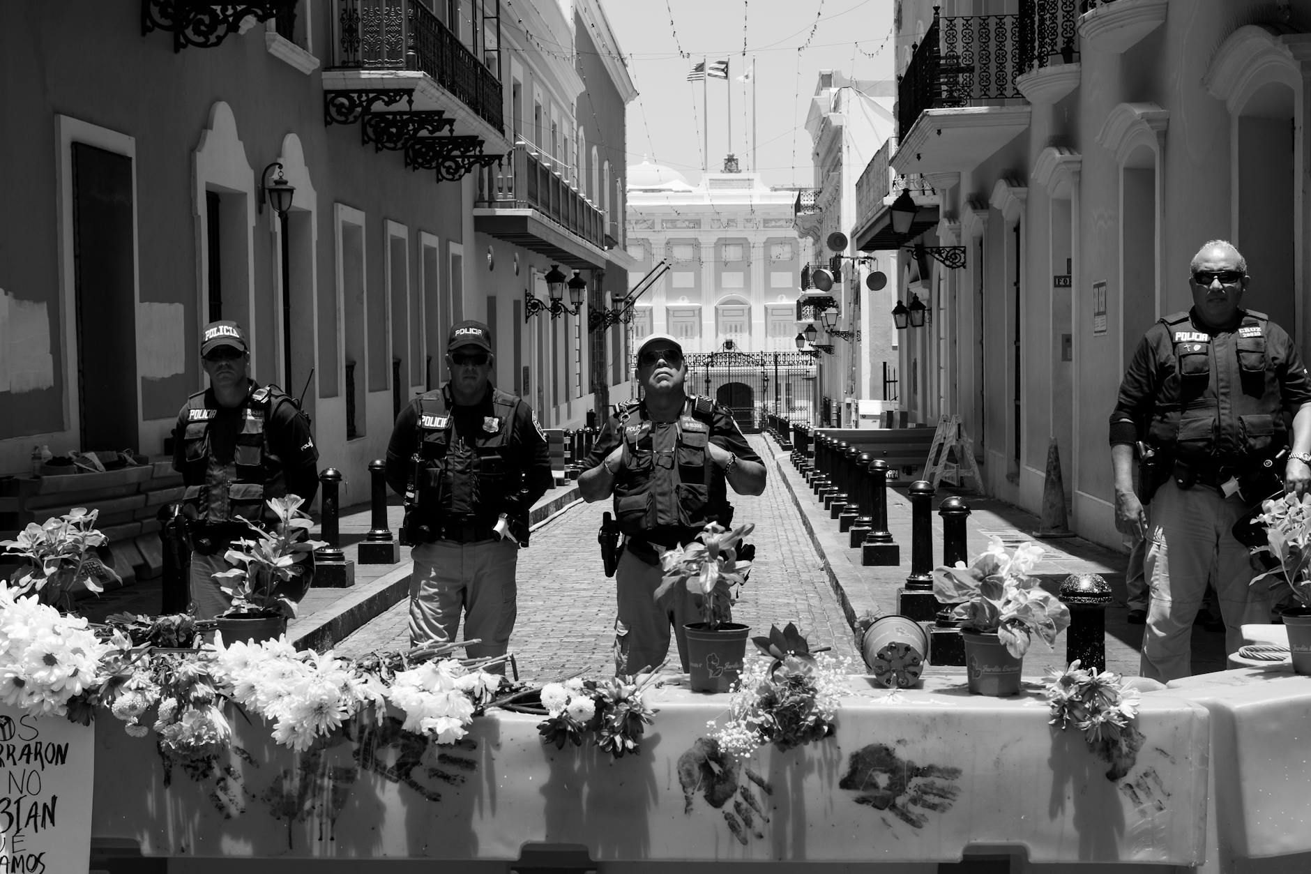 Police officers stand guard behind a flower-adorned barricade on a city street.